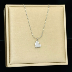 Detail of silver heart pendant necklace displayed on a textured gold jewelry stand