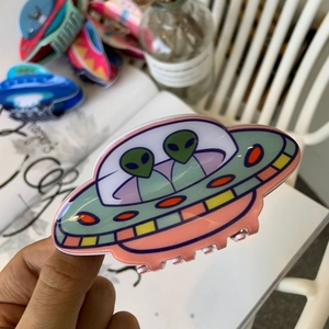 Close-up of acrylic UFO hair claw featuring cute green aliens and retro cartoon design