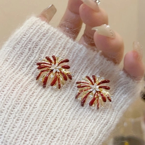 Detailed close-up of red and gold firework-shaped stud earrings held over a sweater