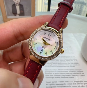 Detail of a gold rhinestone watch with a red leather strap and pearl dial
