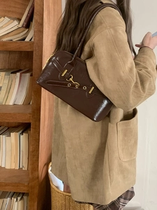 Vintage dark brown patent leather shoulder bag with gold buckle on a model's arm