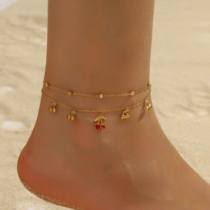 Double-layered gold cherry anklet with sparkling rhinestones worn on a sandy beach