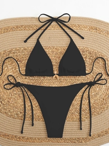Close-up of black bikini set with gold starfish charm on woven beach straw mat
