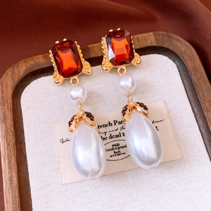 Detailed view of vintage gold earrings with red ruby stones and drop pearls on brown silk
