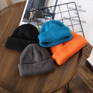 Classic knitted beanies in black, blue, grey, and orange on a minimalist wooden table