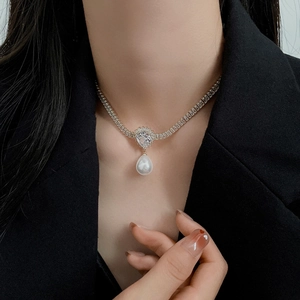 Close-up of gold-plated necklace with white teardrop pearl and sparkling zircon pendant