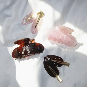 Detailed set of 4 acetate bow hair clips with crystal accents on a white fabric background