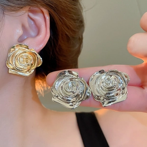 Dettaglio degli orecchini a rosa in metallo oro e argento con trama a rilievo sulla modella