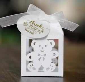 Detail of white laser-cut bear gift box with satin ribbon and thank you tag for parties
