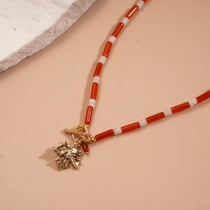 Detailed close-up of handmade beaded necklace with golden maple leaf charm and toggle clasp