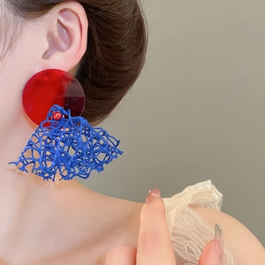Vue détaillée de grandes boucles d'oreilles en maille rouge et bleue portées sur un modèle