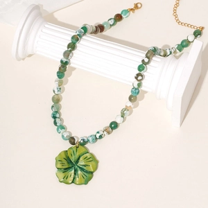 Detail of green flower pendant on marble beads necklace draped over a classic column
