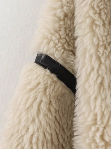 Detail of off-white faux shearling fabric texture with black leather trim and strap