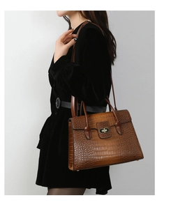 Detail of brown crocodile pattern handbag with gold clasp worn over a black coat