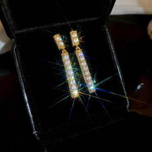 Detailed view of golden rectangular earrings with sparkling zircons in a black box