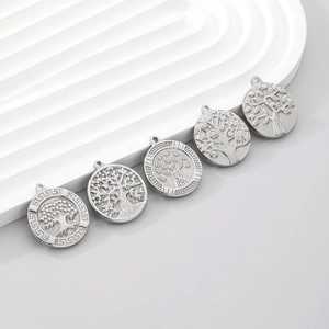 Detail of five silver stainless steel tree of life charms on a white display stand