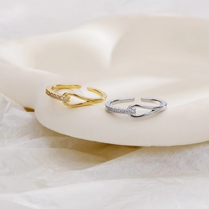 Detailed close-up of gold and silver knotted zircon rings on a beige ceramic tray