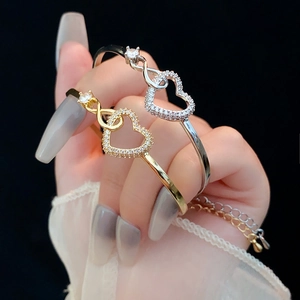 Detail of gold and silver heart infinity bracelets with sparkling zircons on wrist