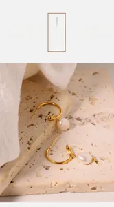 Detailed close-up of gold baroque pearl drop earrings on a textured stone surface