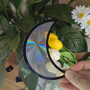 Close-up of a moon-shaped suncatcher with rainbow holographic effects held outdoors