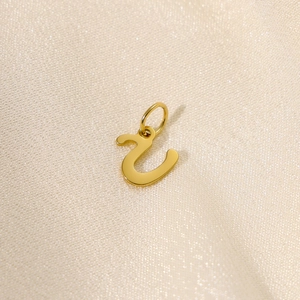 Detail of gold-plated stainless steel initial pendant on elegant beige silk fabric
