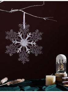 Close-up of a large transparent acrylic snowflake ornament hanging on a frosted branch