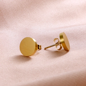 Close-up of golden flat circular stud earrings on soft pink satin fabric with brushed finish