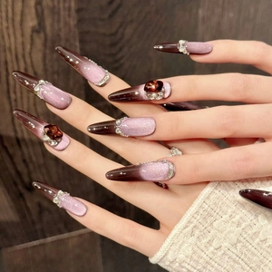 Detail van stiletto plaknagels met paars kattenoogeffect en amberkleurige stenen