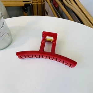 Detail view of a glossy red large hair claw clip with a golden spring on a white surface
