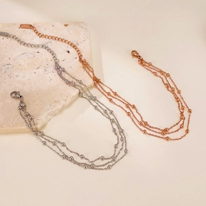 Detail of layered silver and rose gold beaded anklets on textured stone surface