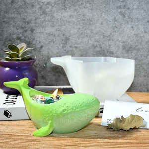 Detail view of a whale-shaped silicone mold with a finished green candle and seashell accents