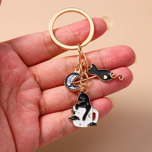 Detail of a gold keychain with black cat in cup and heart enamel charms on pink background
