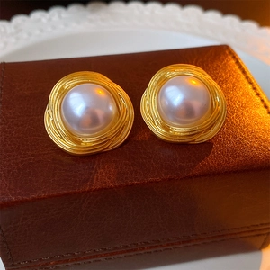 Détail de boucles d'oreilles perles vintage avec design nid doré sur un écrin en cuir