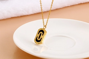 Detail shot of a golden oval pendant with a black C-shaped inlay on a paperclip chain