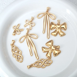 Golden stainless steel bow and knot pendants displayed in a white ceramic dish
