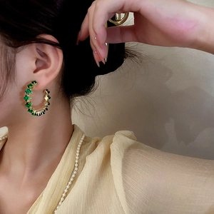 Vintage C-shaped gold hoop earrings with emerald green crystals on a female model