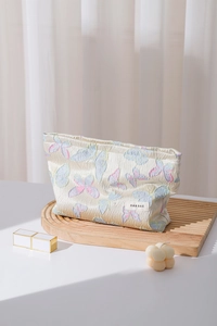 Detailansicht der beigen Kosmetiktasche mit bunter Schmetterlingsstickerei und Logo