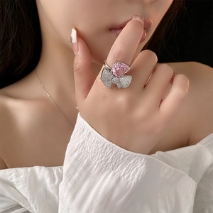 Gros plan d'une bague avec pierre rose en forme de cœur et nìud sur le doigt