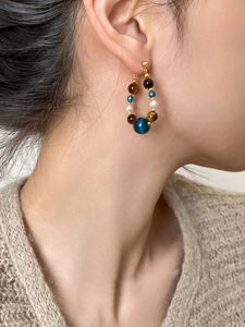 Détail d'une boucle d'oreille en perles d'œil de tigre et perles portée par un mannequin