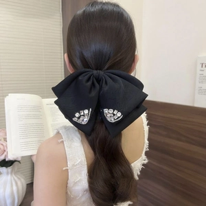 Detail of large black satin bow hair claw clip with sparkling rhinestones on model