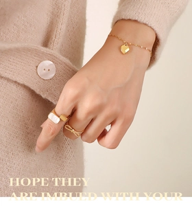 Detailed close-up of gold heart pendant bracelet and gemstone rings on model's hand