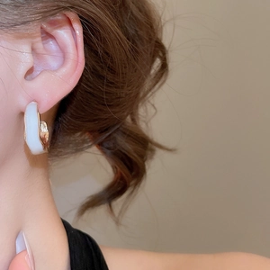 Detail of C-shaped earring with white enamel and golden textured metal on ear