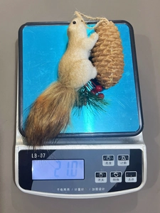 Close-up of squirrel ornament with pine cone and berries weighing 21 grams on a scale