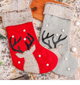 Detail of red and grey plush Christmas stockings with reindeer motifs on snowy wood