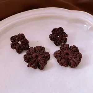Handmade dark brown woven flower drop earrings on a white ceramic display tray