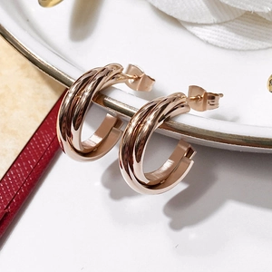 Detail of rose gold triple-intertwined hoop earring on a white ceramic plate