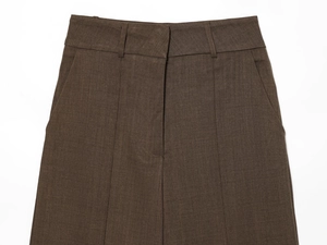 Detail of high-waist dark brown trousers showing waist straps and slanted pocket craftsmanship