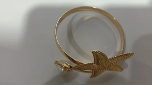 Detailed close-up of golden starfish arm cuff with white pearl and textured shell detail