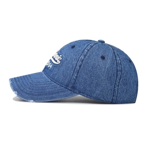 Macro detail of washed blue denim cap featuring white 1984 embroidery and distressed edges
