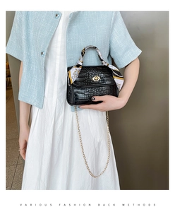 Detail of black croc-embossed handbag with gold clasp and decorative silk scarf wrap